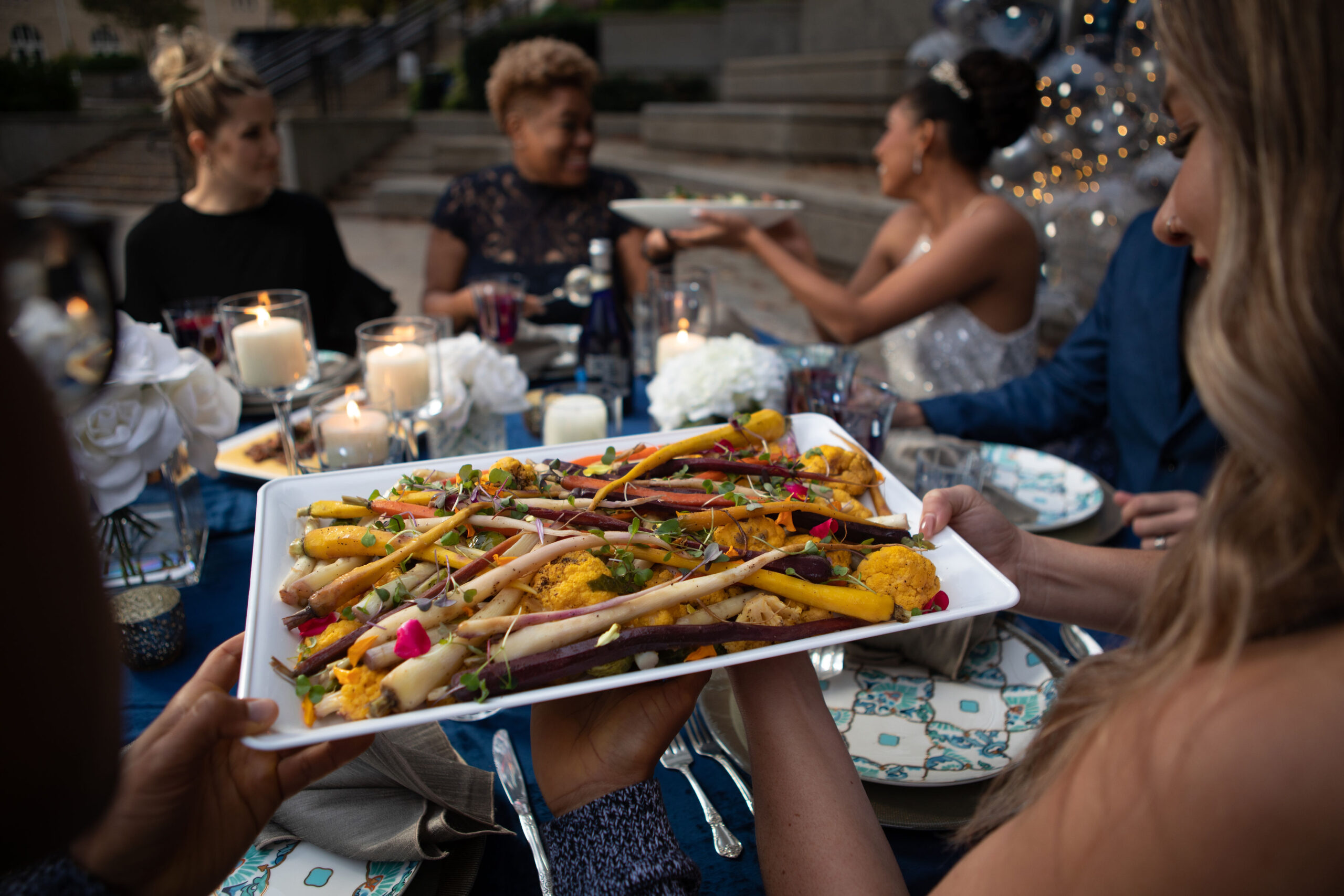 Picture of wedding reception in the outdoor plaza with a closeup of roasted vegetables.