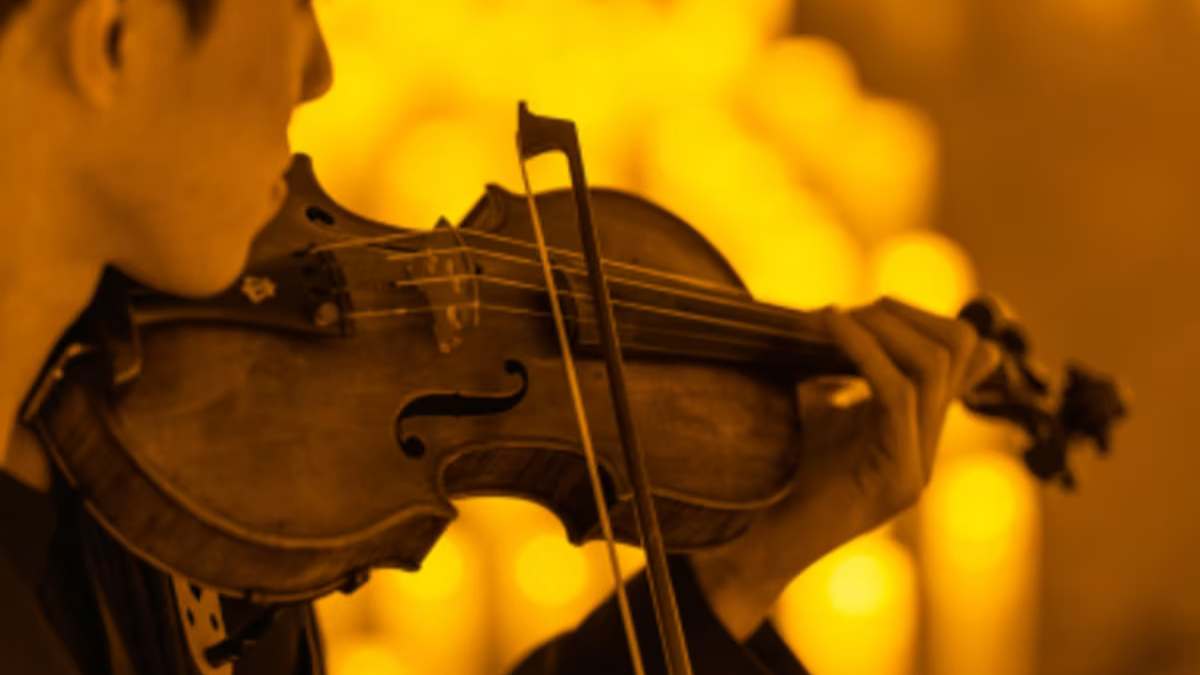 Close-up of a musician playing a violin during a Candlelight: Christmas Carols on Strings concert, with thousands of blurred warm glowing candles creating a soft golden background bokeh.